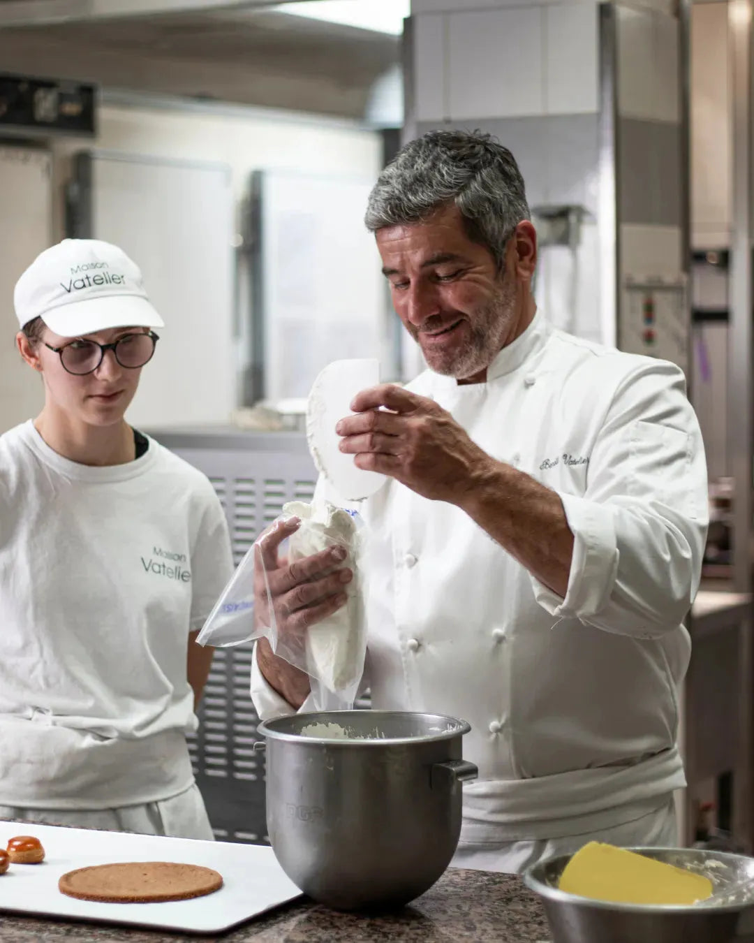 Un pâtissier en tenue blanche travaillant une pâte dans un laboratoire de pâtisserie.