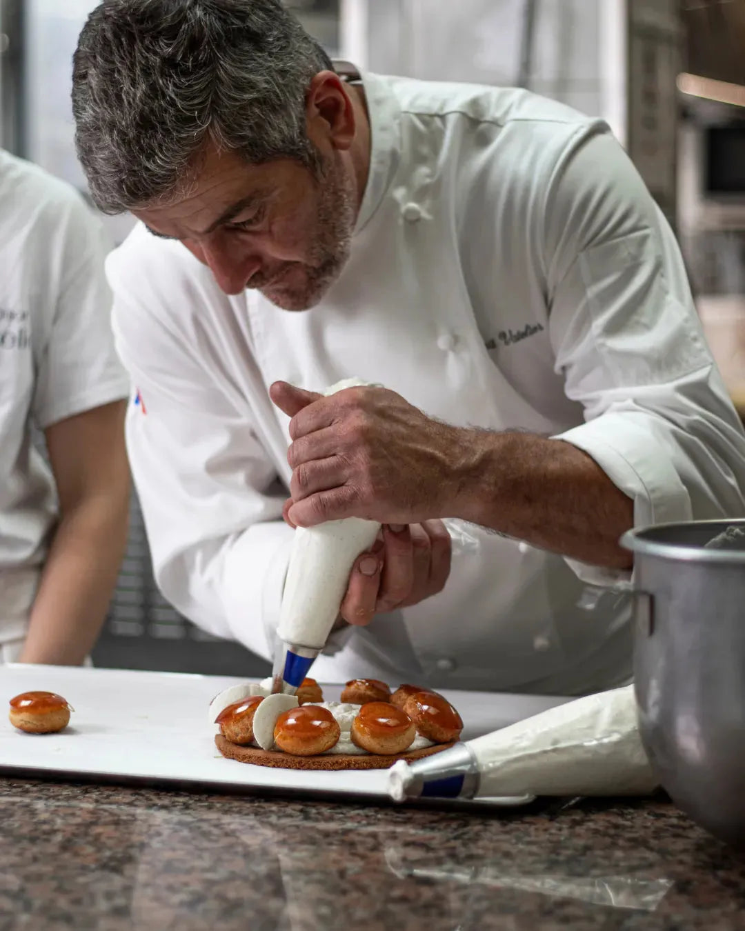 Pâtissier décorant avec précision un entremets avec une poche à douille.