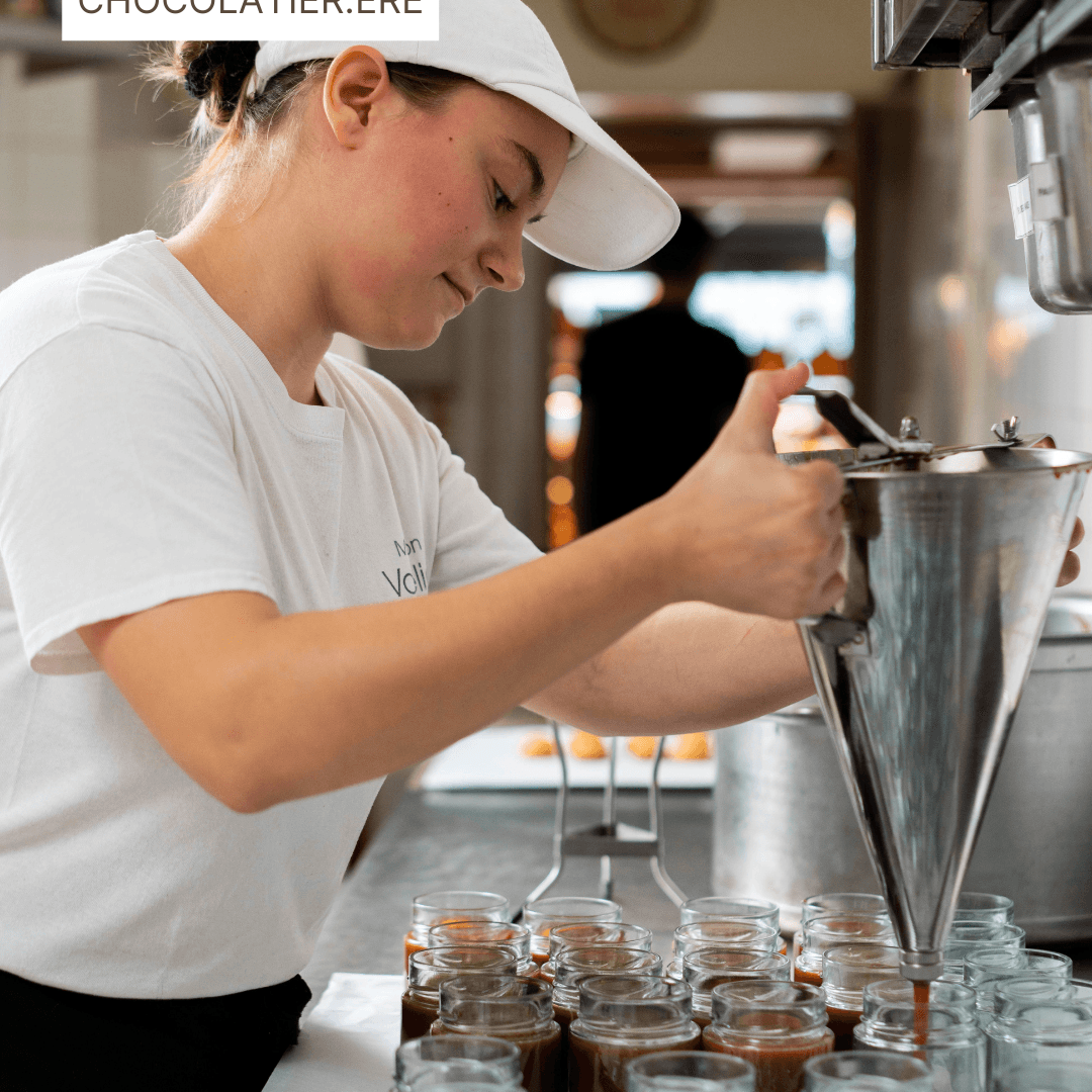 Une chocolatière remplissant des pots de caramel avec un entonnoir en acier inoxydable.