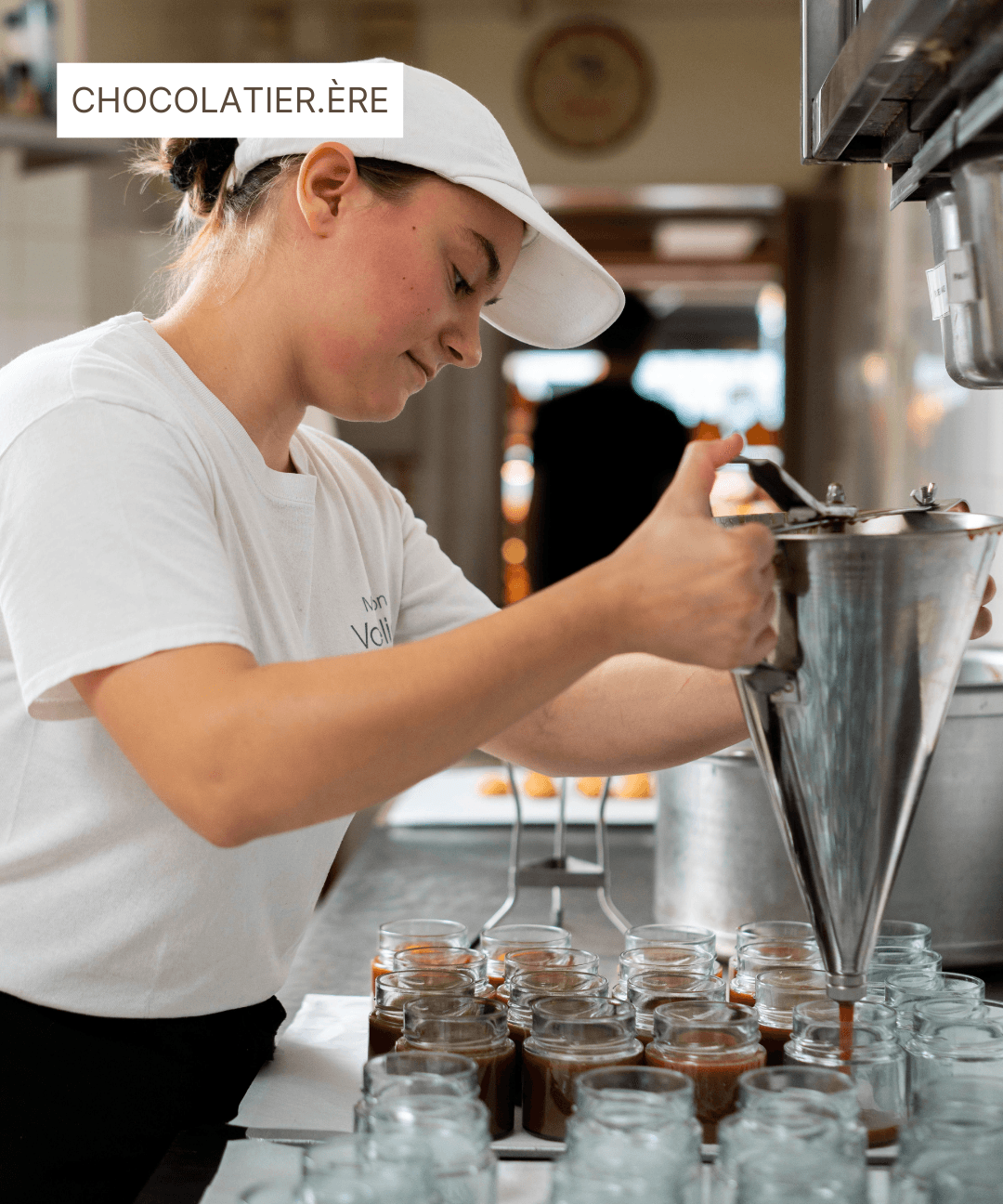 Une chocolatière remplissant des pots de caramel avec un entonnoir en acier inoxydable.