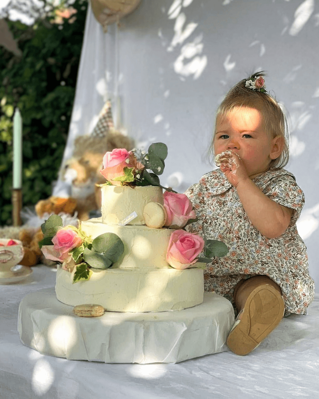 Bébé goûtant un gâteau d'anniversaire blanc décoré de roses roses.