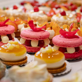 Assortiment de mignardises : macarons roses aux framboises et tartelettes aux fruits exotiques.