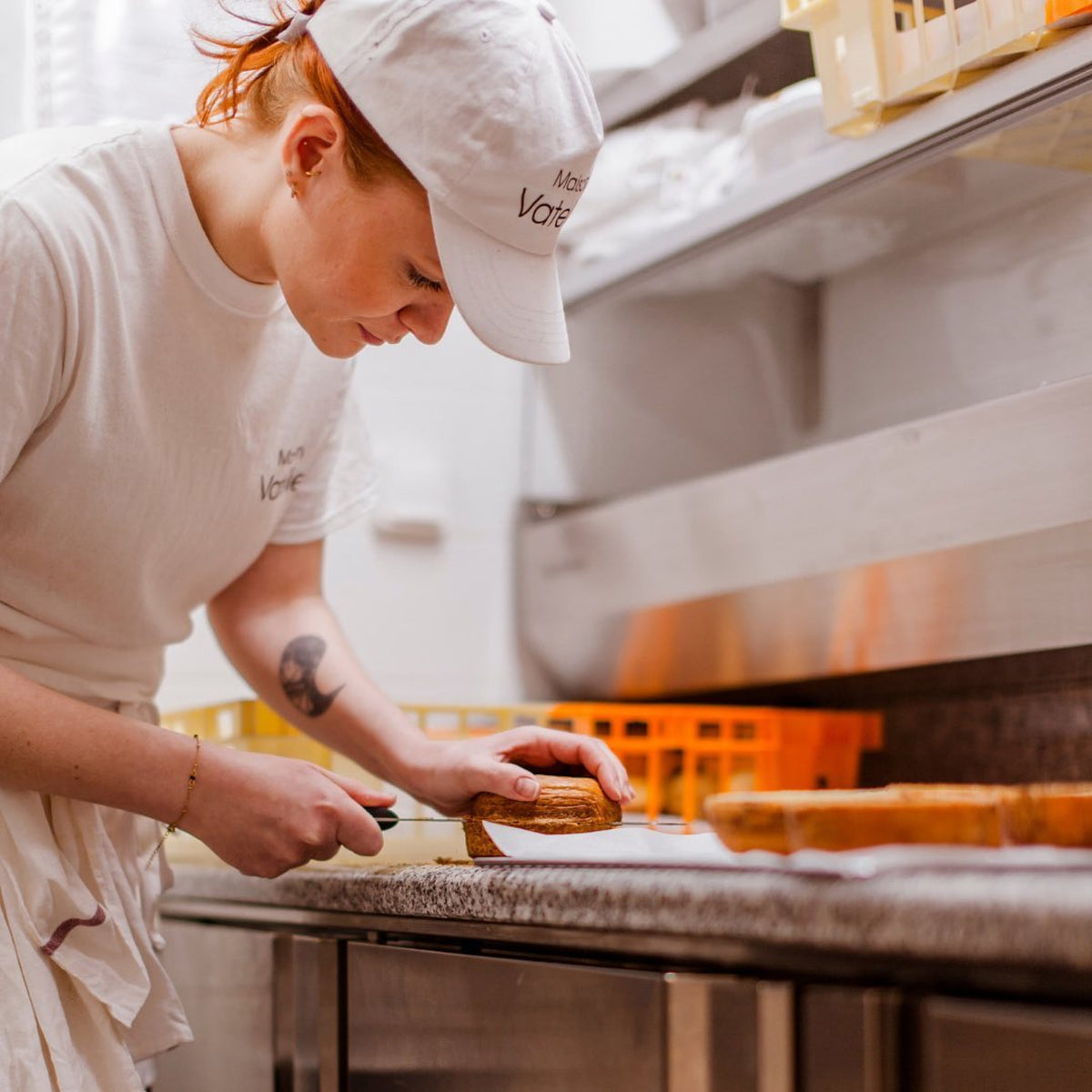 Une pâtissière découpe avec précision un gâteau dans un atelier de pâtisserie.