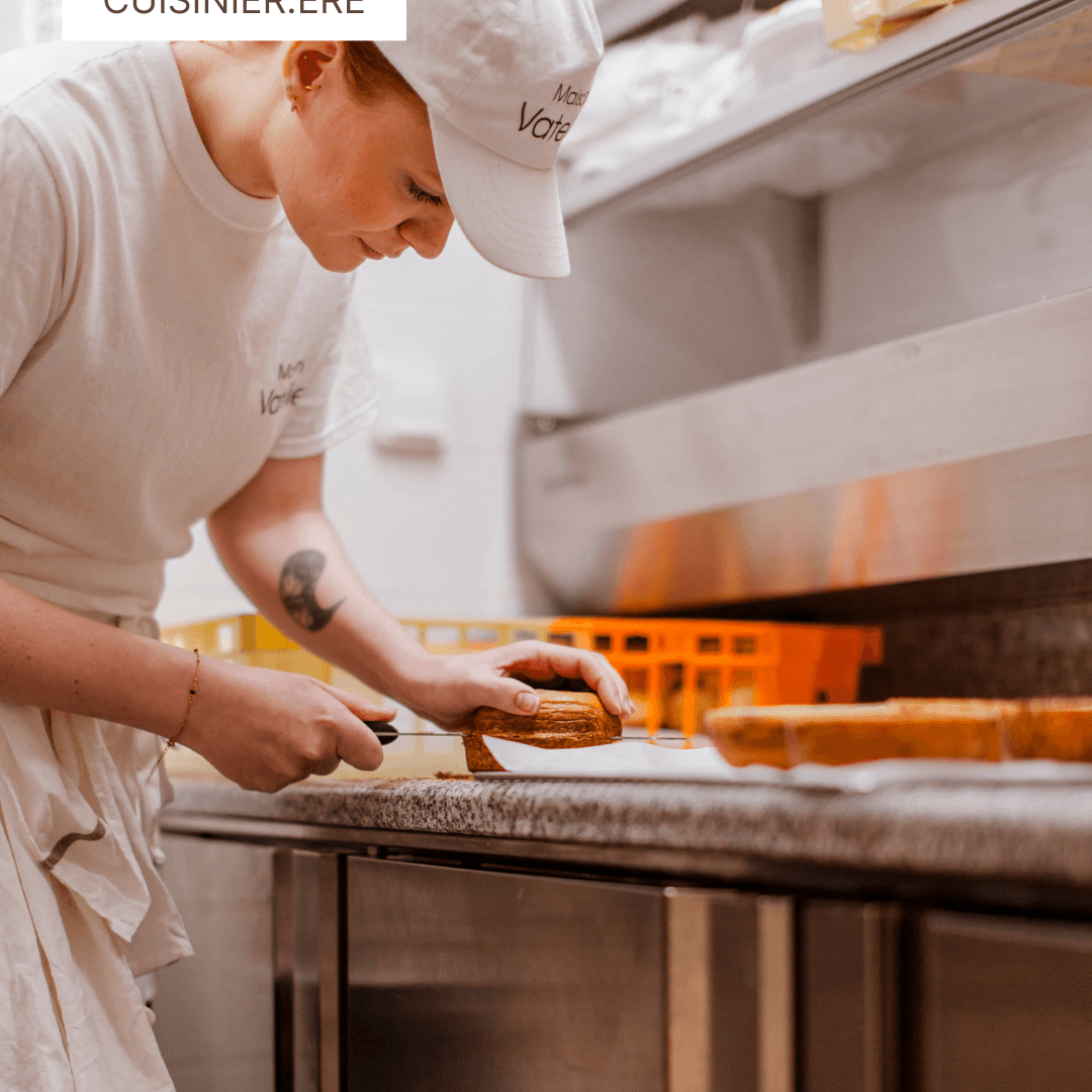 Cuisinière en tenue blanche découpant avec précision un gâteau dans un atelier de pâtisserie.