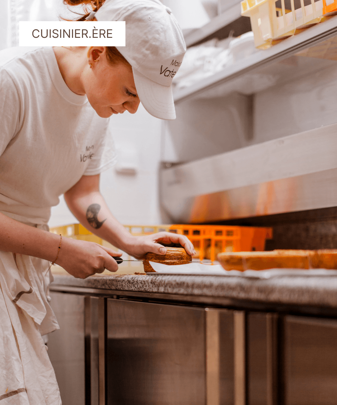 Cuisinière en tenue blanche découpant avec précision un gâteau dans un atelier de pâtisserie.