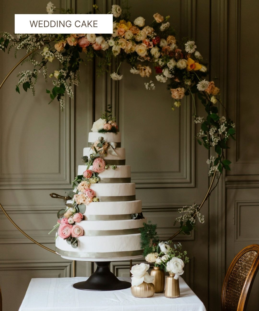 Gâteau de mariage blanc à plusieurs étages décoré de fleurs fraîches et de rubans gris.
