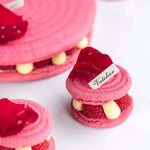 Macarons roses Maison Vatelier garnis de framboises et crème, décorés de pétales de fleurs.
