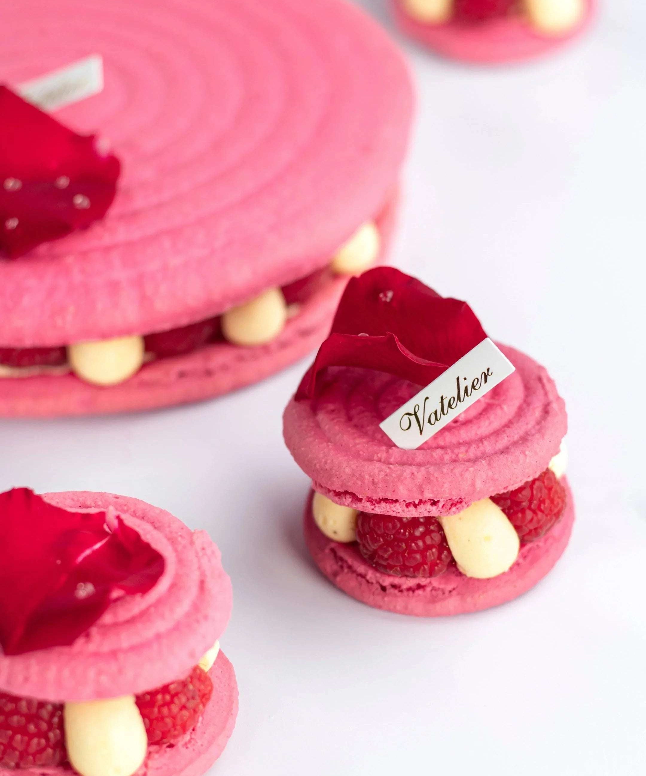 Macarons roses Maison Vatelier garnis de framboises et crème, décorés de pétales de fleurs.
