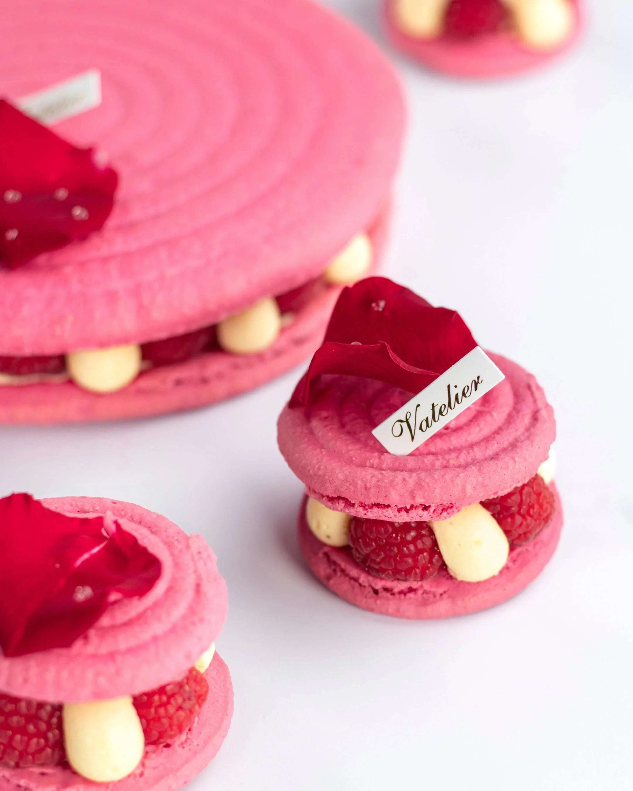 Macarons roses Maison Vatelier garnis de framboises et crème, décorés de pétales de fleurs.