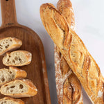 Baguettes de tradition Maison Vatelier, entières et tranchées sur une planche en bois.
