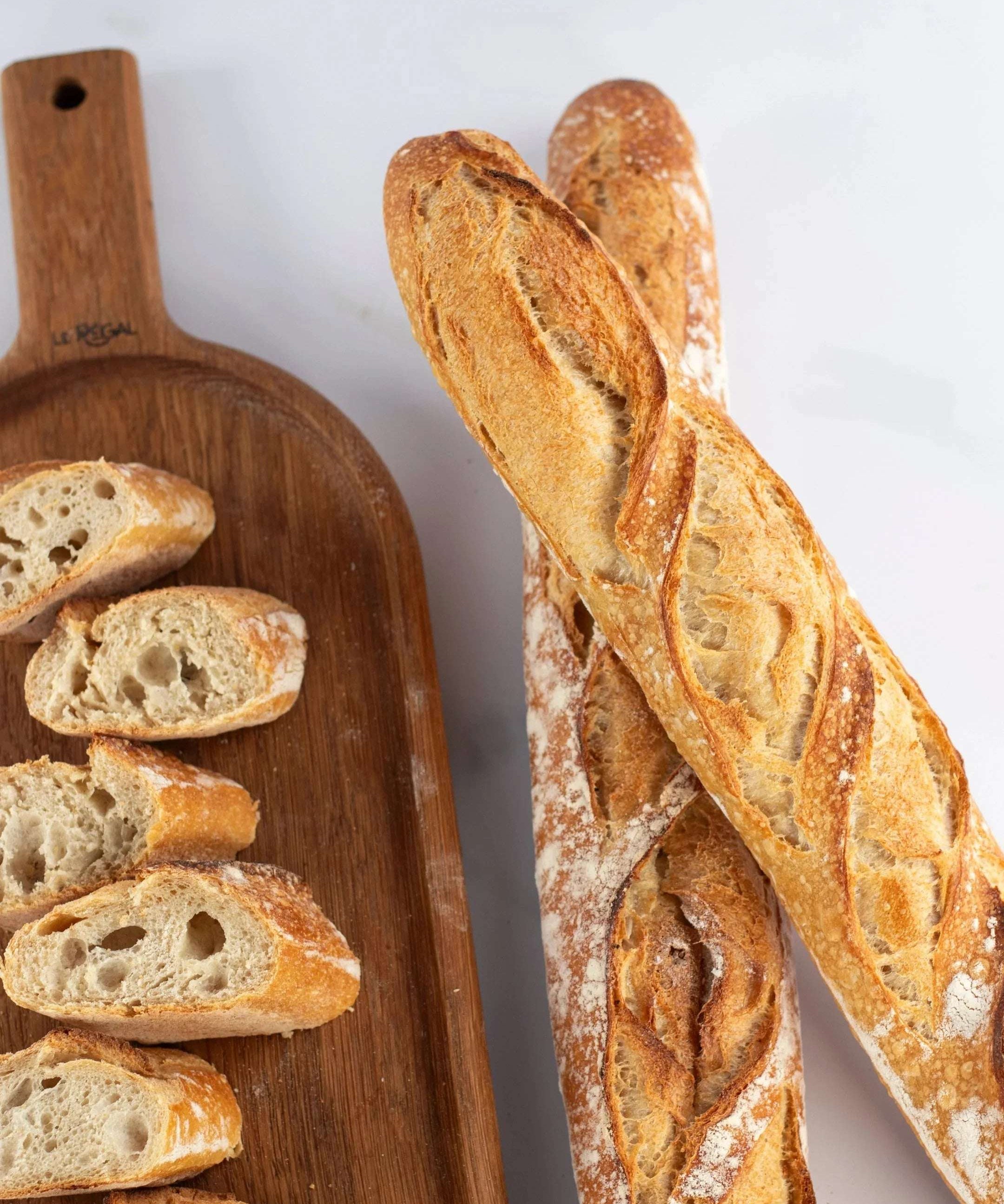 Baguettes de tradition Maison Vatelier, entières et tranchées sur une planche en bois.