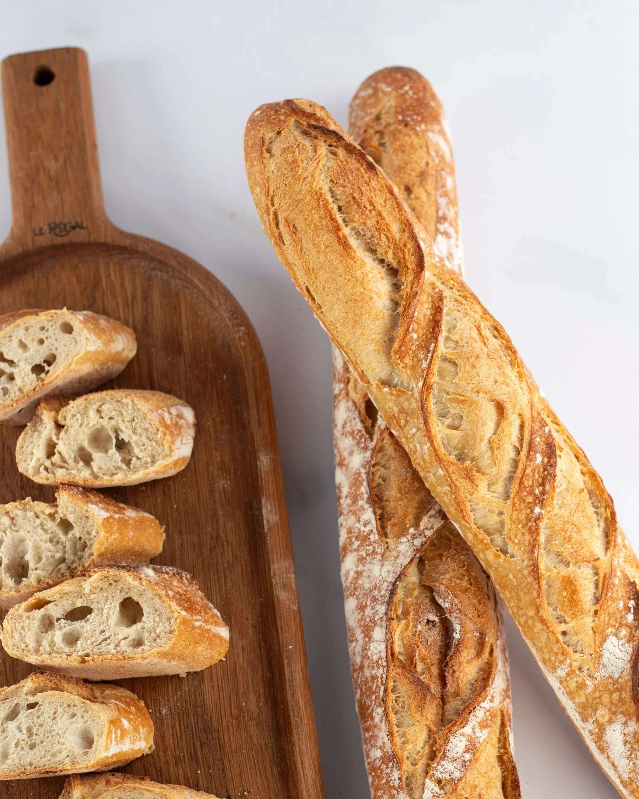 Baguettes de tradition Maison Vatelier, entières et tranchées sur une planche en bois.