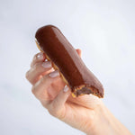 Main tenant un éclair au chocolat Maison Vatelier avec une bouchée.