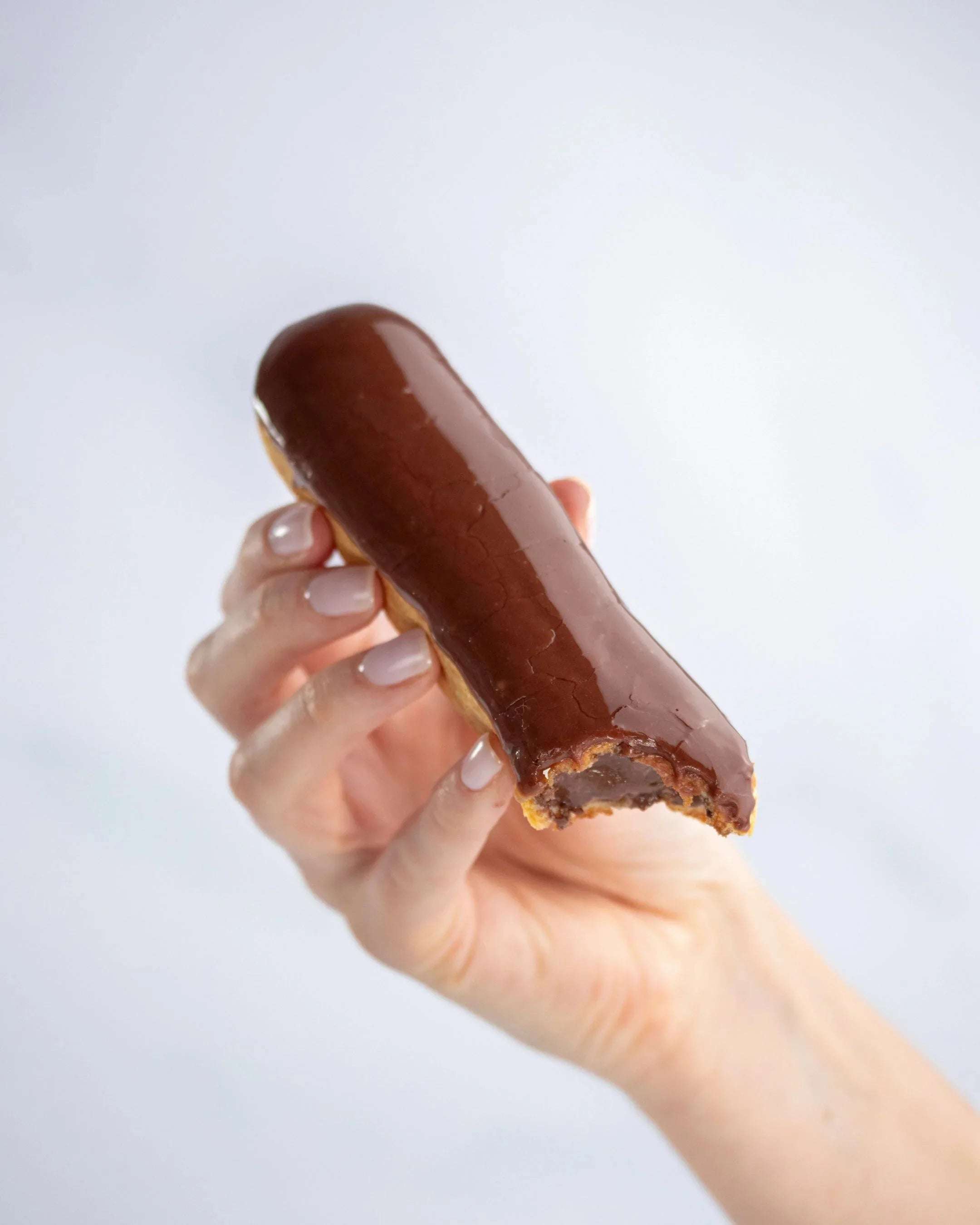 Main tenant un éclair au chocolat Maison Vatelier avec une bouchée.