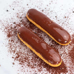 Deux éclairs au chocolat Maison Vatelier sur un fond blanc saupoudré de cacao.
