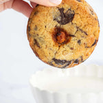 Main tenant un cookie 3 chocolats Maison Vatelier au-dessus d'un bol de lait blanc.