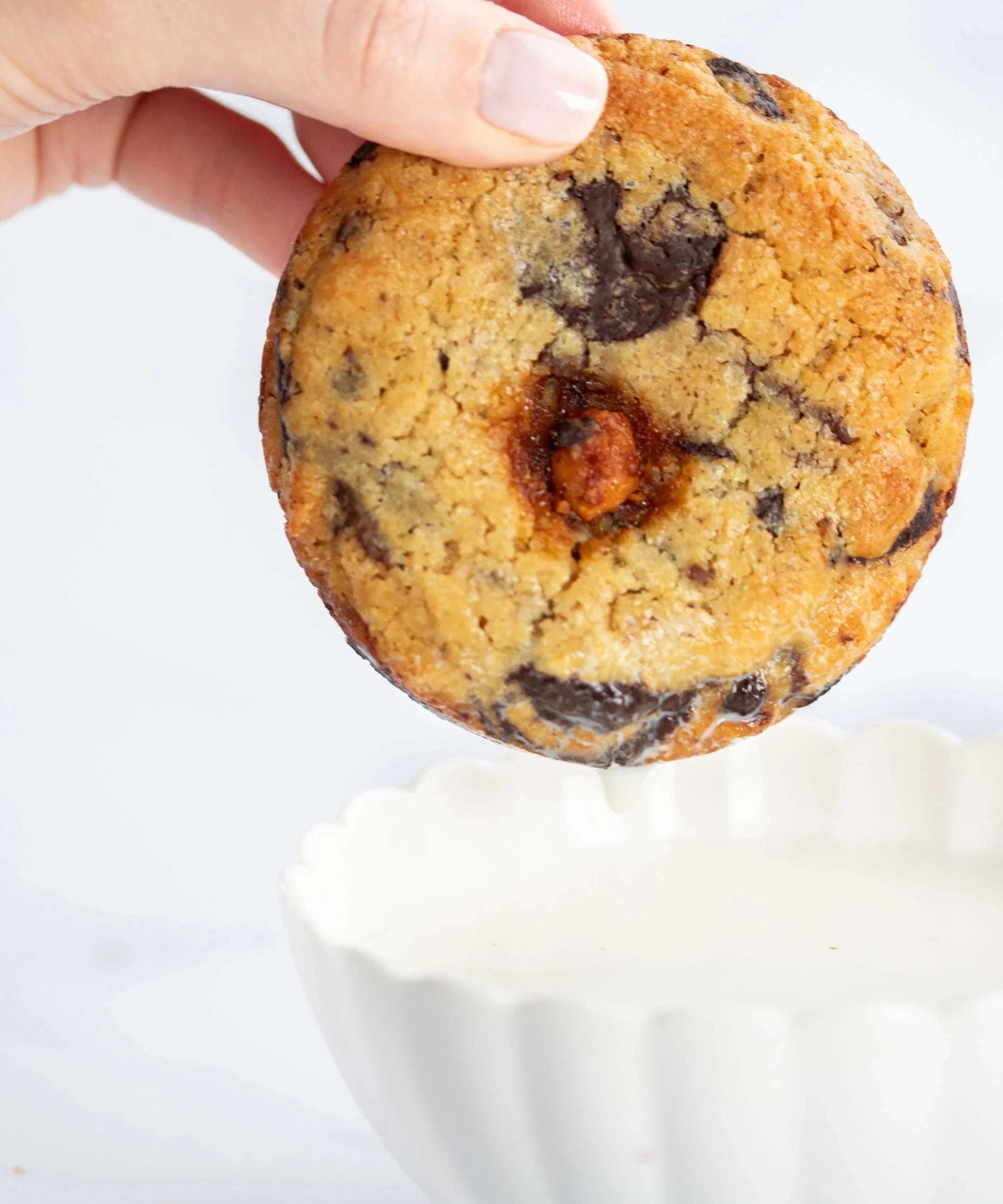Main tenant un cookie 3 chocolats Maison Vatelier au-dessus d'un bol de lait blanc.