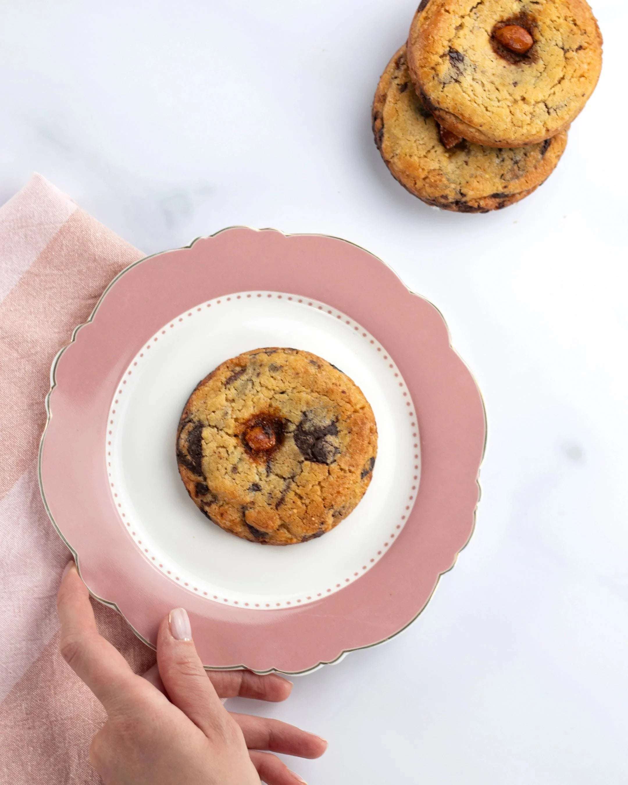 Cookie 3 Chocolats de Maison Vatelier sur une assiette rose avec des cookies en arrière-plan.