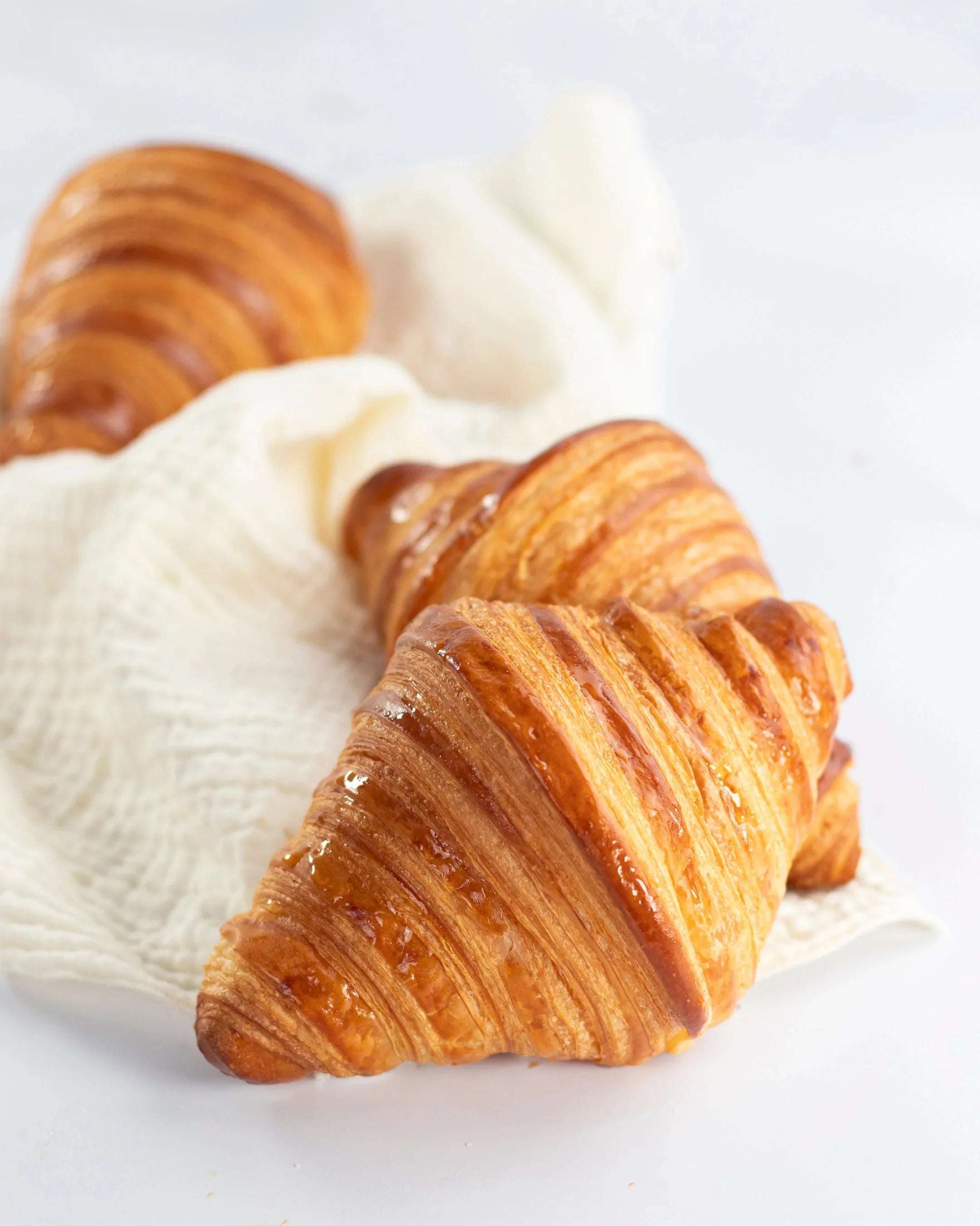 Trois croissants Maison Vatelier dorés et croustillants posés sur un linge blanc.