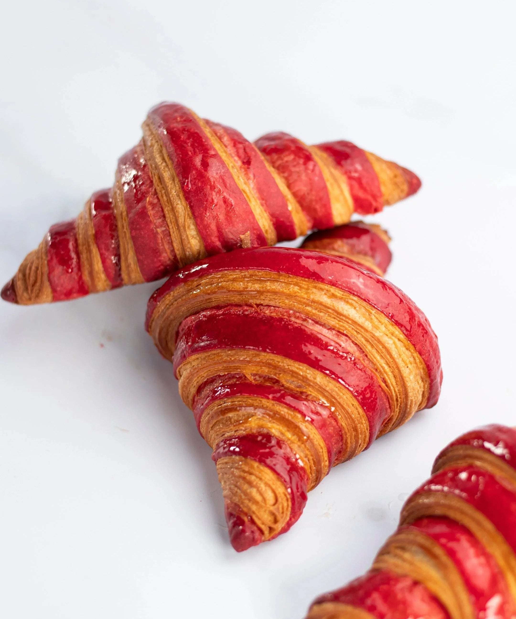 Gros plan de croissants à la framboise Maison Vatelier avec glaçage rouge brillant.