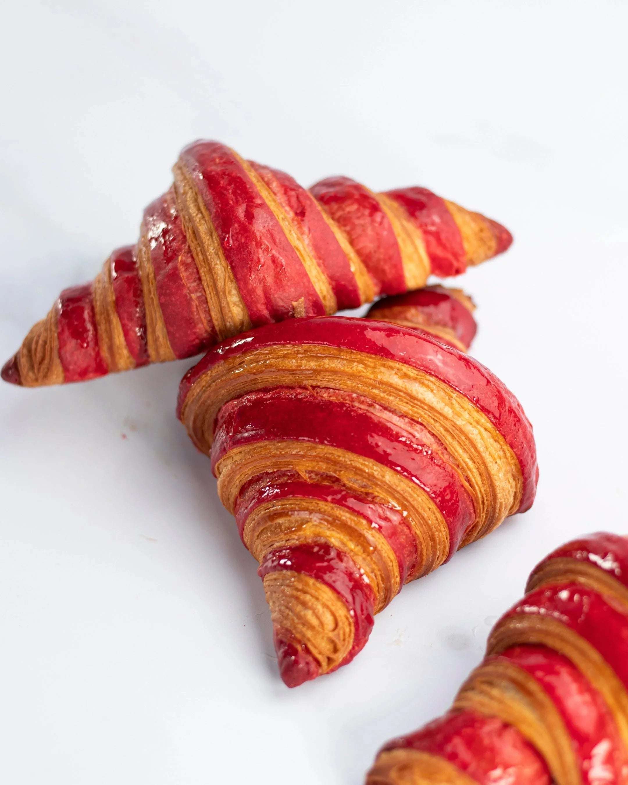 Gros plan de croissants à la framboise Maison Vatelier avec glaçage rouge brillant.