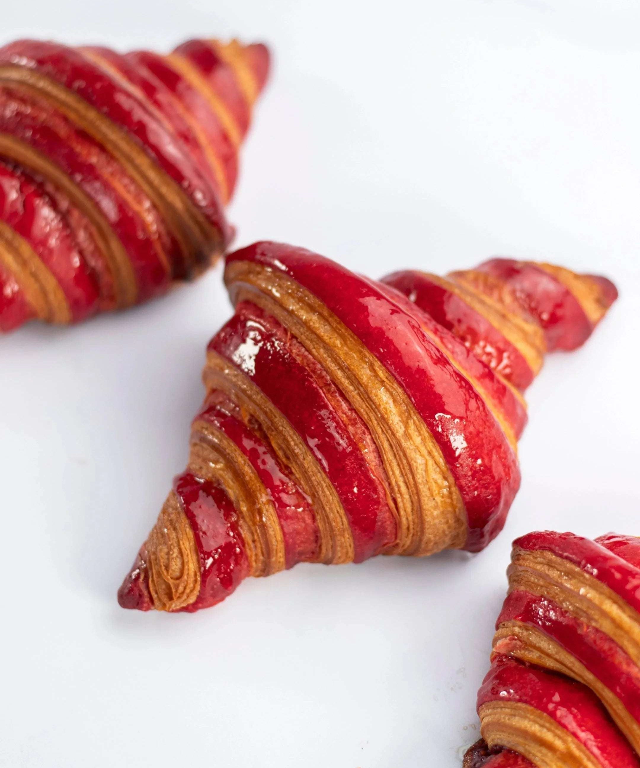 Gros plan de croissants Maison Vatelier nappés de glaçage framboise rouge brillant