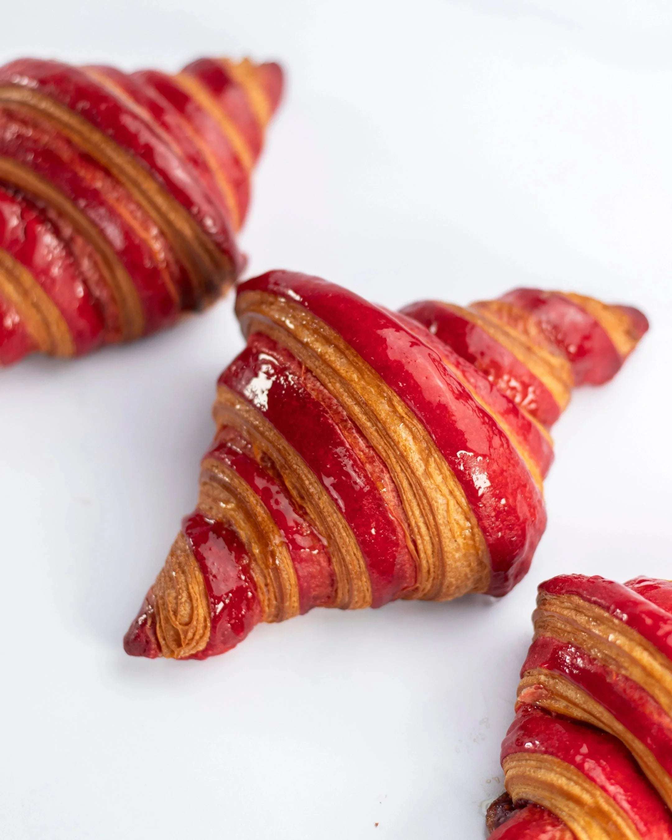 Gros plan de croissants Maison Vatelier nappés de glaçage framboise rouge brillant