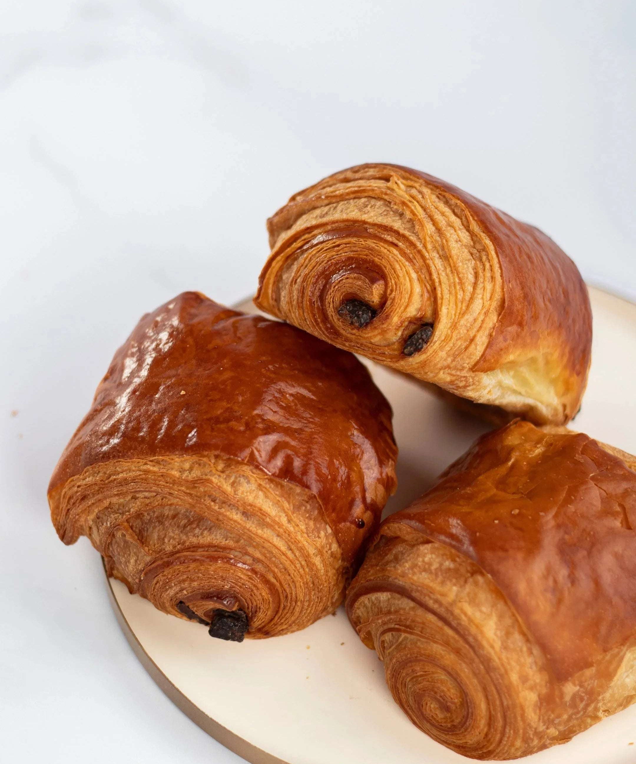 Trois pains au chocolat feuilletés et dorés Maison Vatelier sur un plateau blanc.