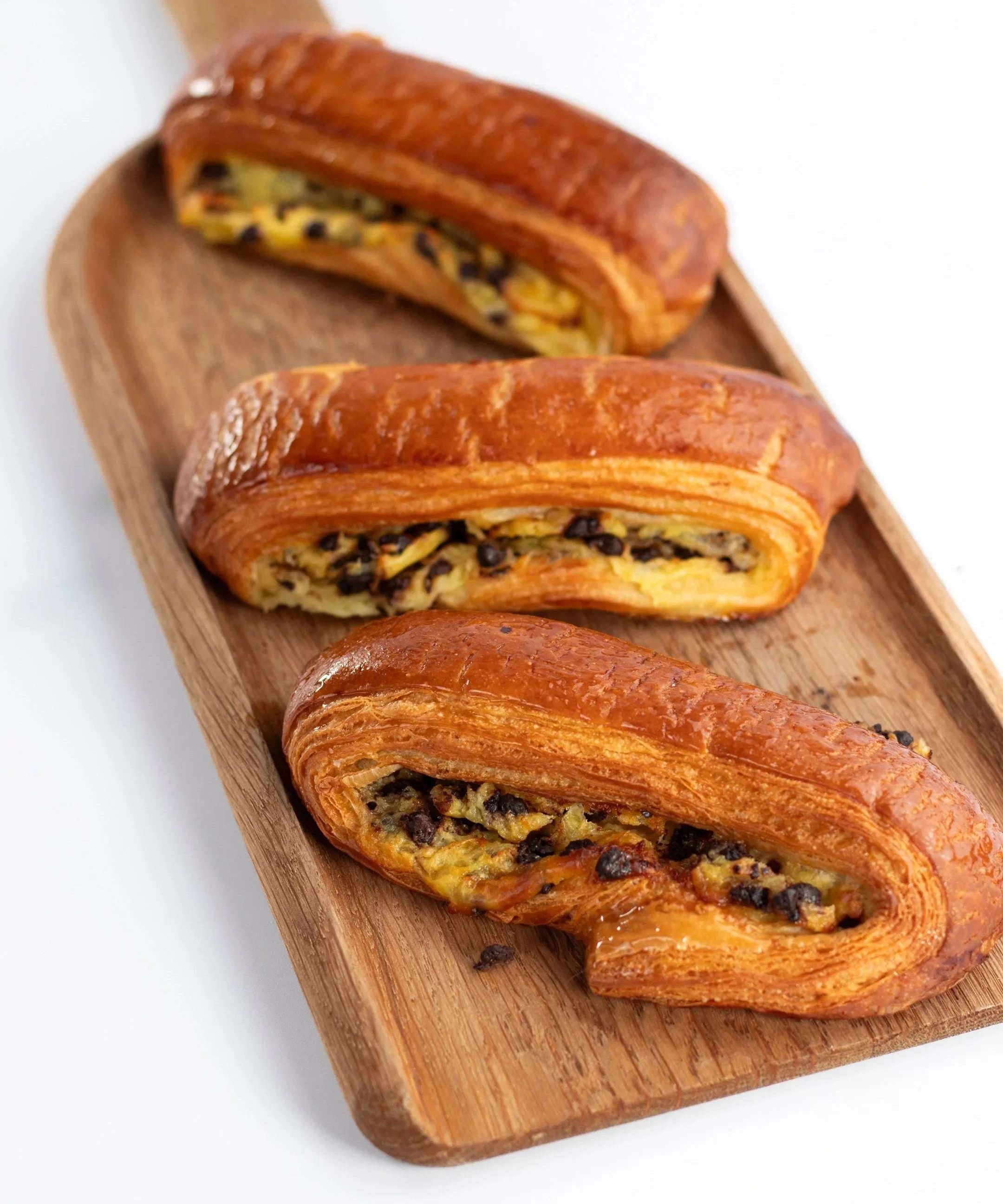 Trois viennoiseries feuilletées aux pépites de chocolat Maison Vatelier sur un plateau en bois.