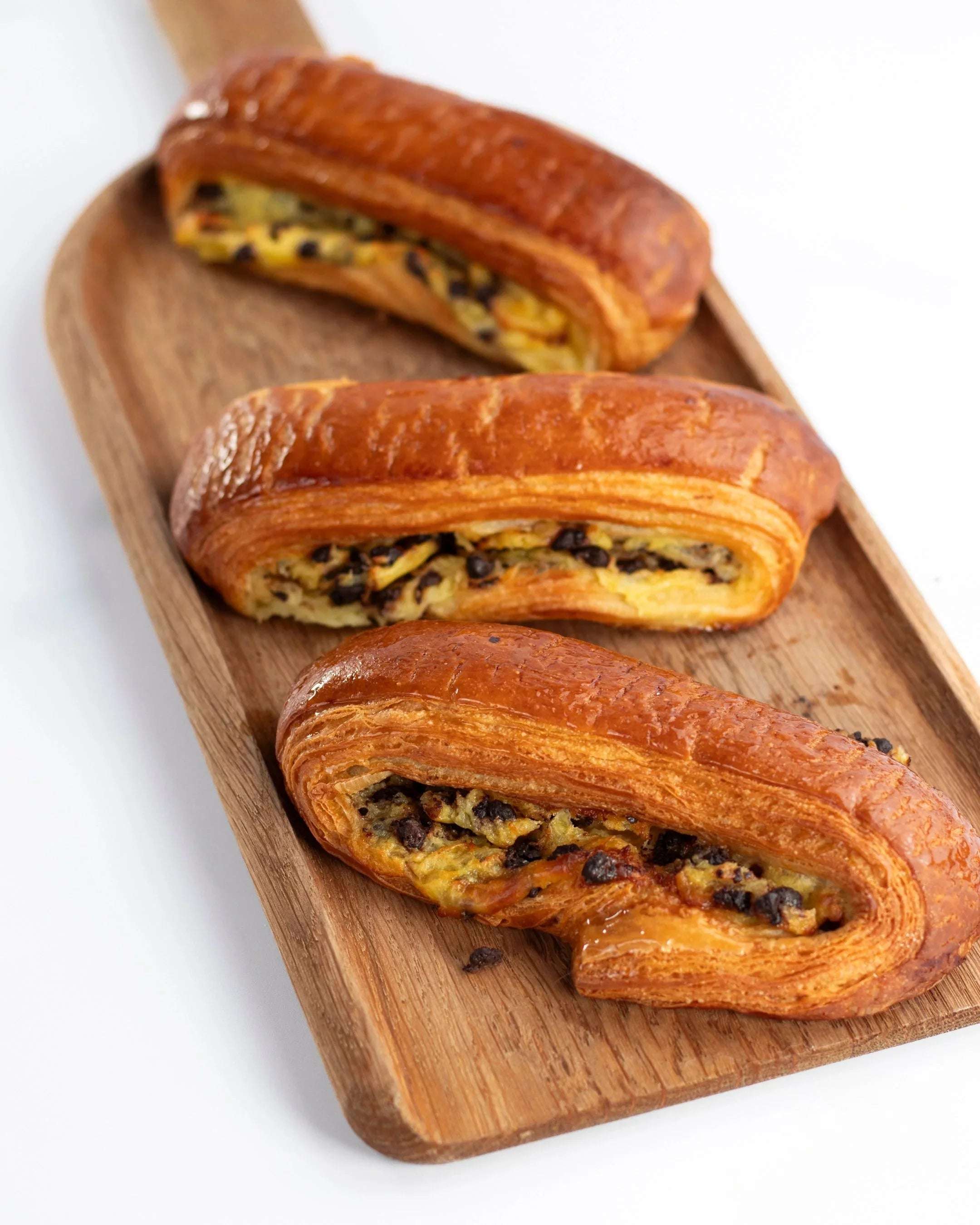 Trois viennoiseries feuilletées aux pépites de chocolat Maison Vatelier sur un plateau en bois.