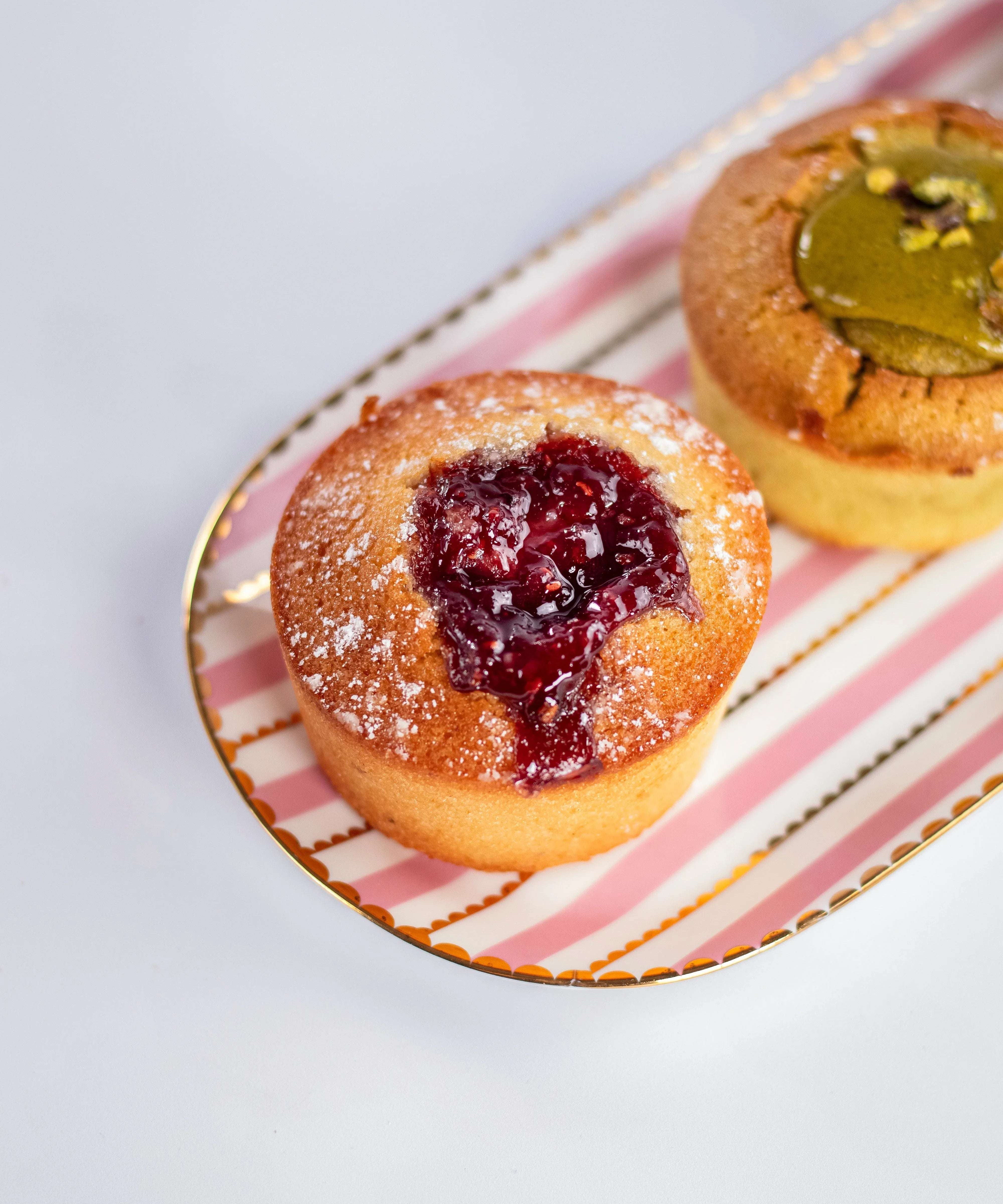 Financier à la framboise saupoudré de sucre glace de Maison Vatelier sur un plateau rayé.