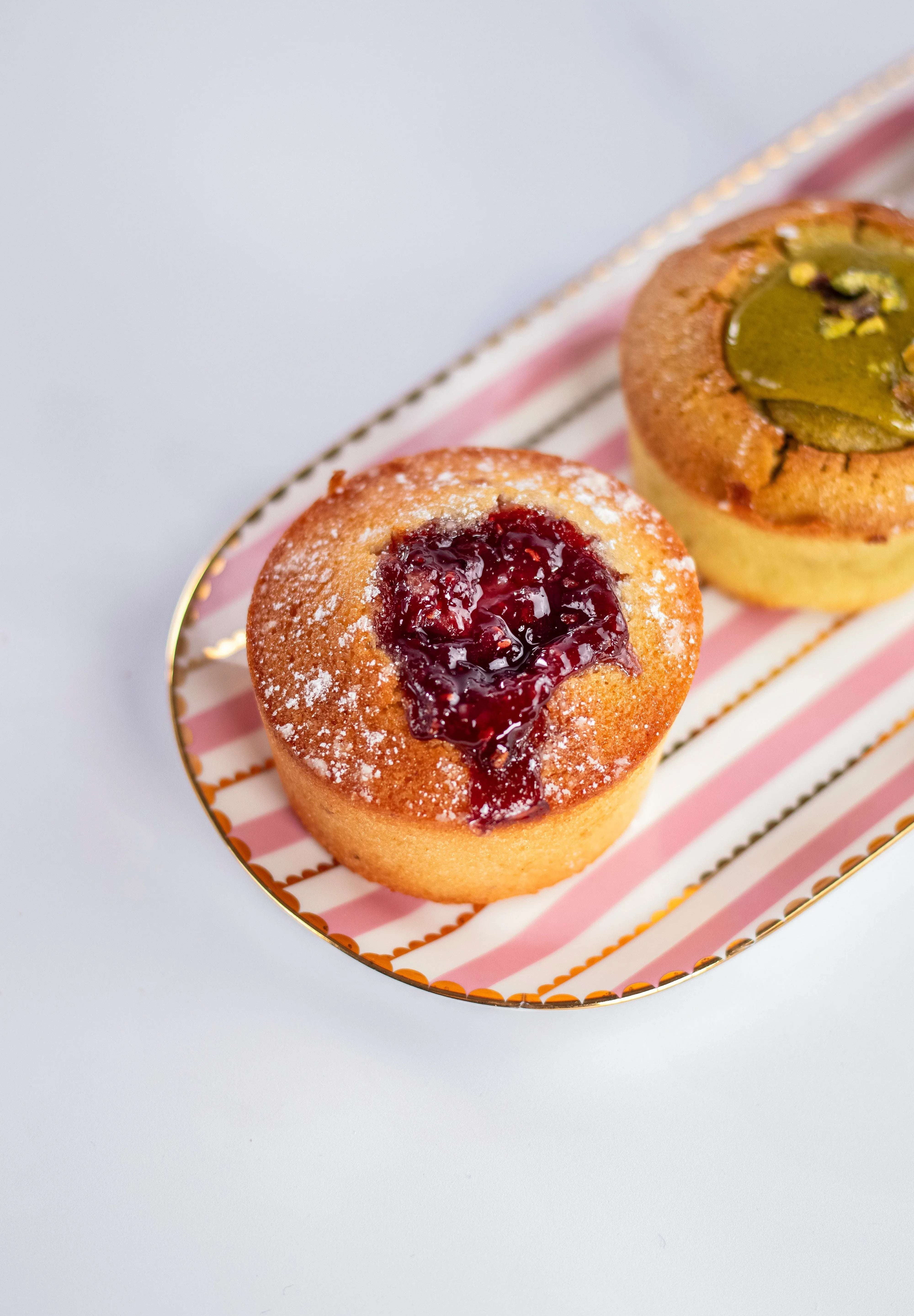 Financier à la framboise saupoudré de sucre glace de Maison Vatelier sur un plateau rayé.