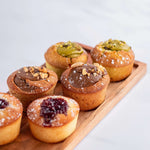 Assortiment de gâteaux de voyage Maison Vatelier, dont un financier framboise, sur plateau bois.