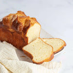 Brioche Longue Maison Vatelier dorée et moelleuse, tranchée sur un linge blanc.