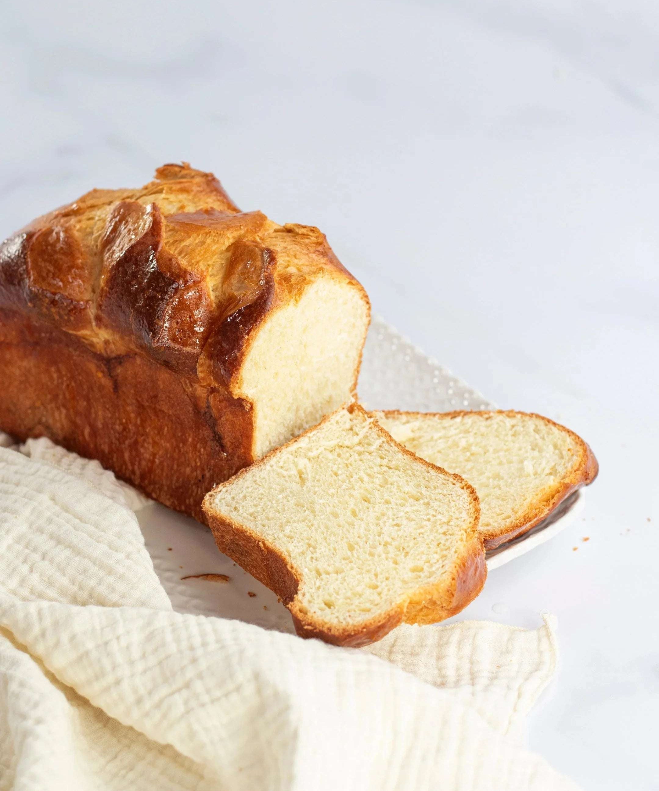 Brioche Longue Maison Vatelier dorée et moelleuse, tranchée sur un linge blanc.