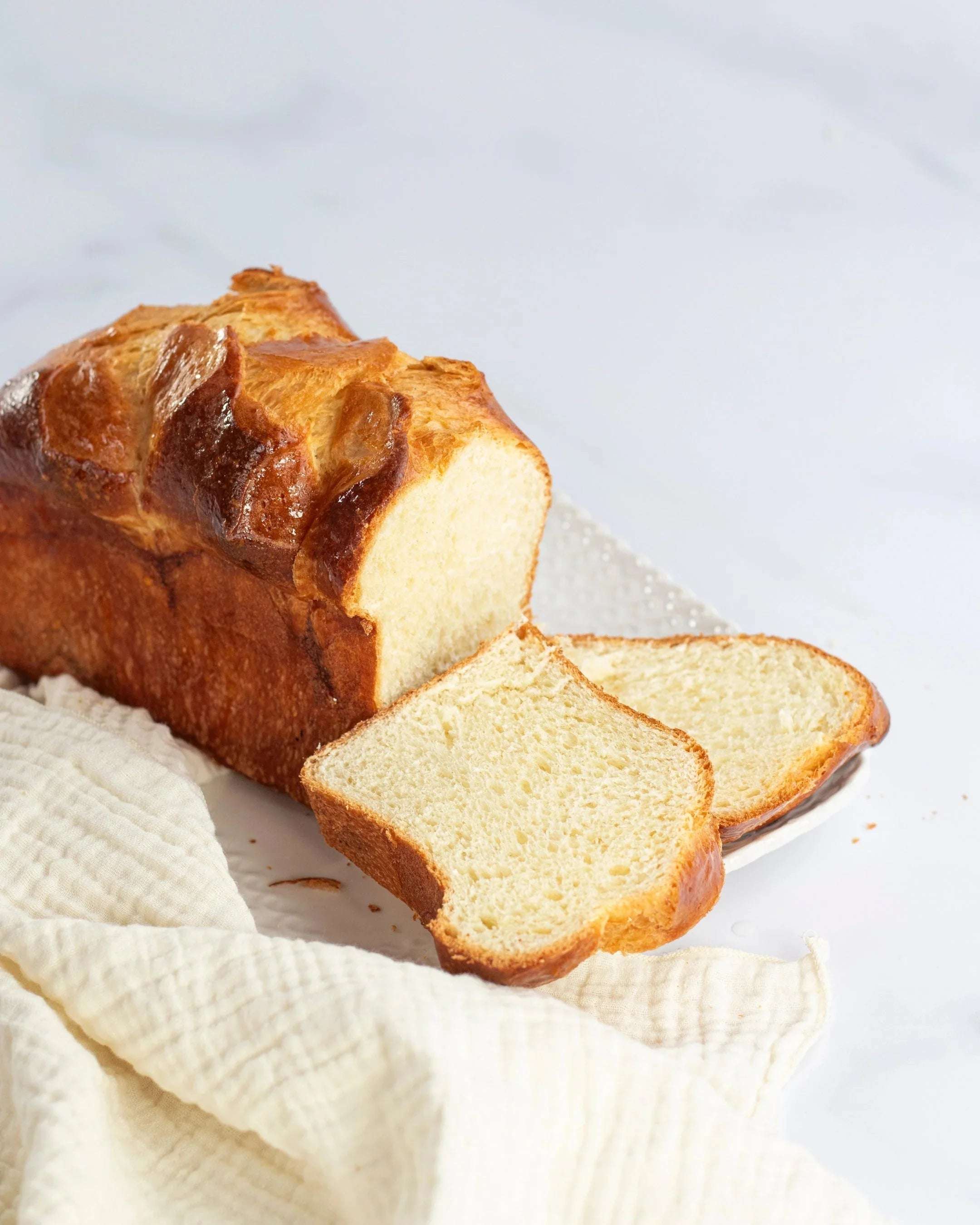 Brioche Longue Maison Vatelier dorée et moelleuse, tranchée sur un linge blanc.