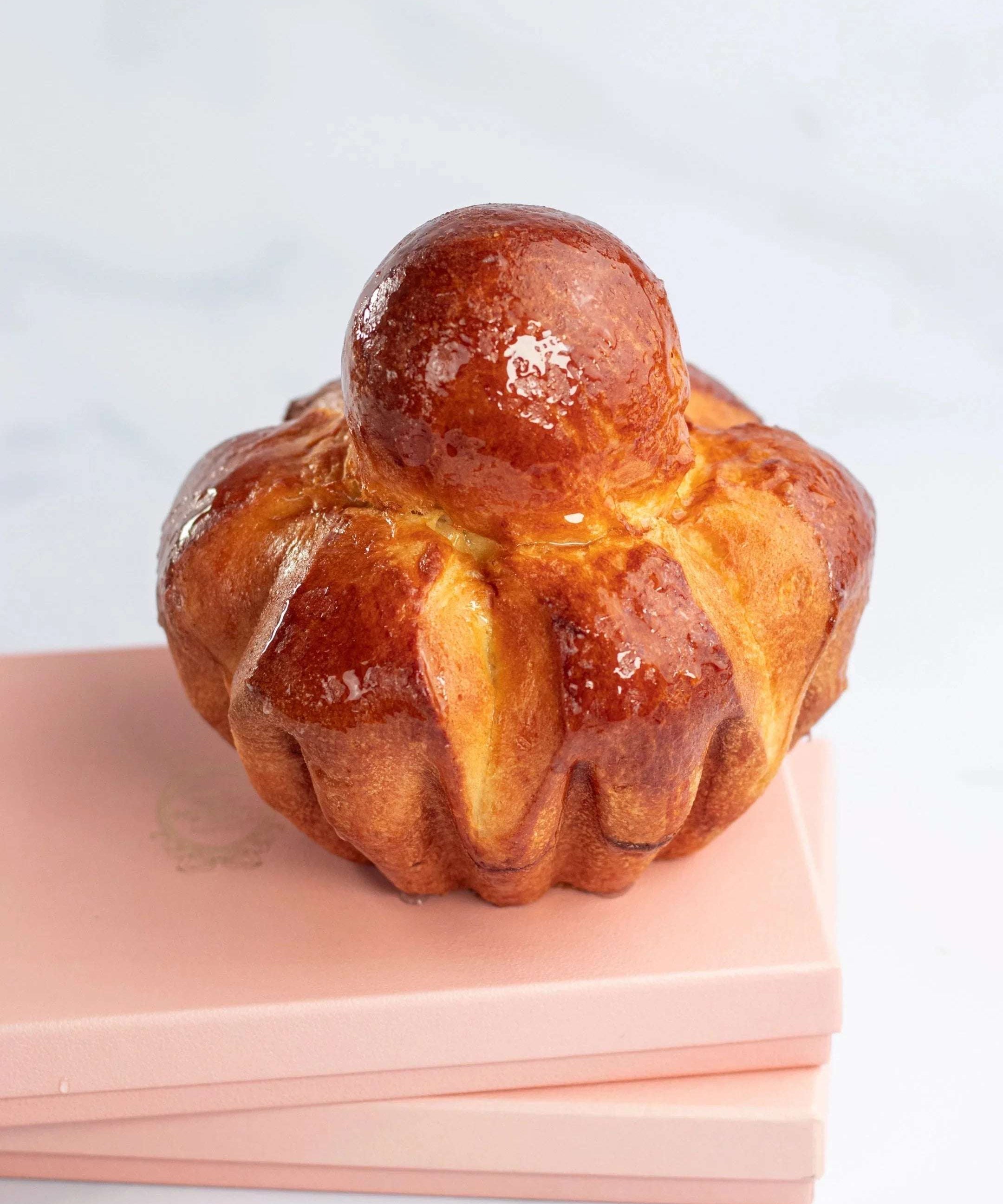 Brioche Parisienne dorée et brillante de Maison Vatelier sur un support rose.