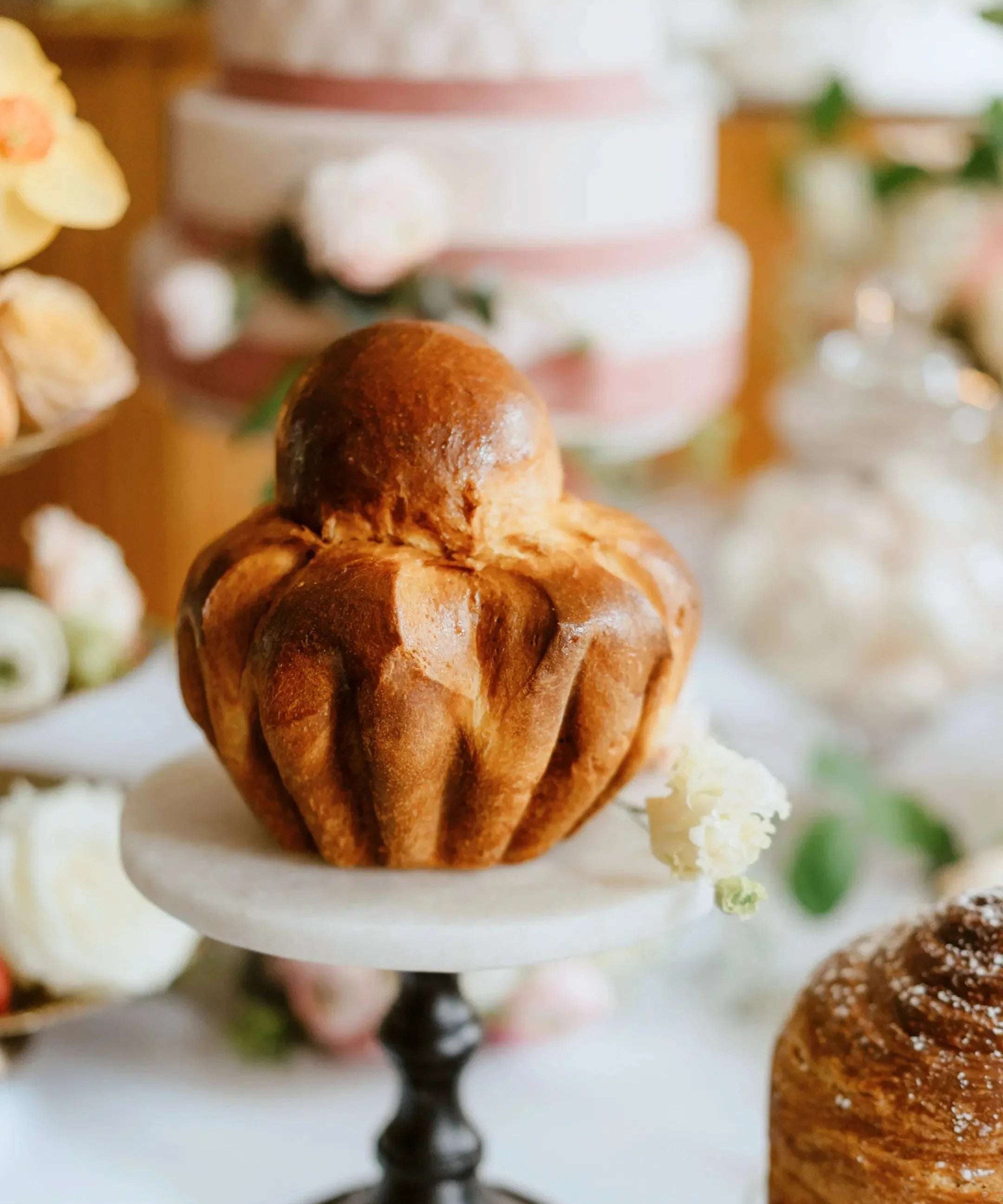 Brioche Parisienne dorée Maison Vatelier sur un présentoir blanc entourée de fleurs