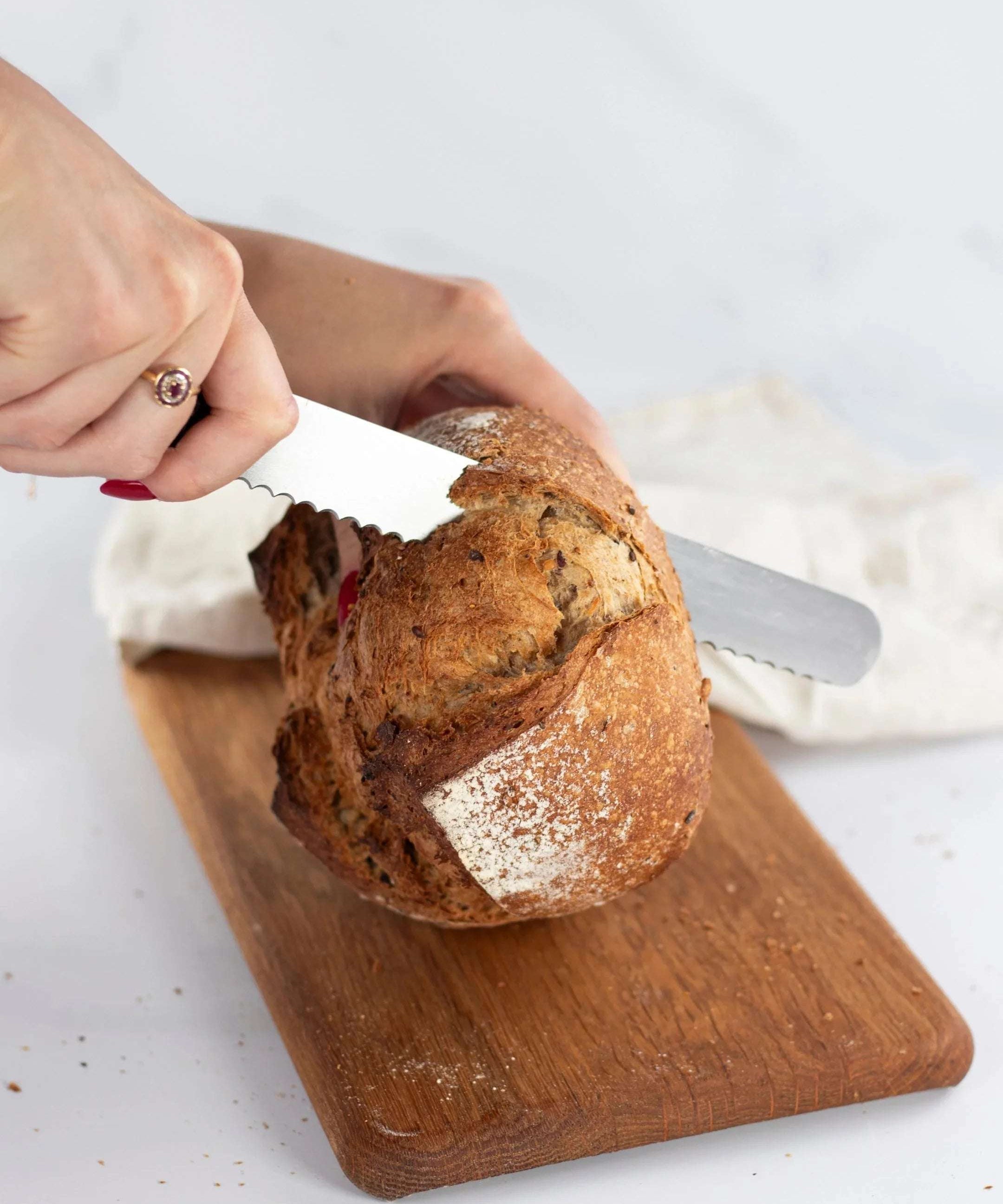 Une personne coupe un pain Bûcheron de Maison Vatelier avec un couteau à pain sur une planche.