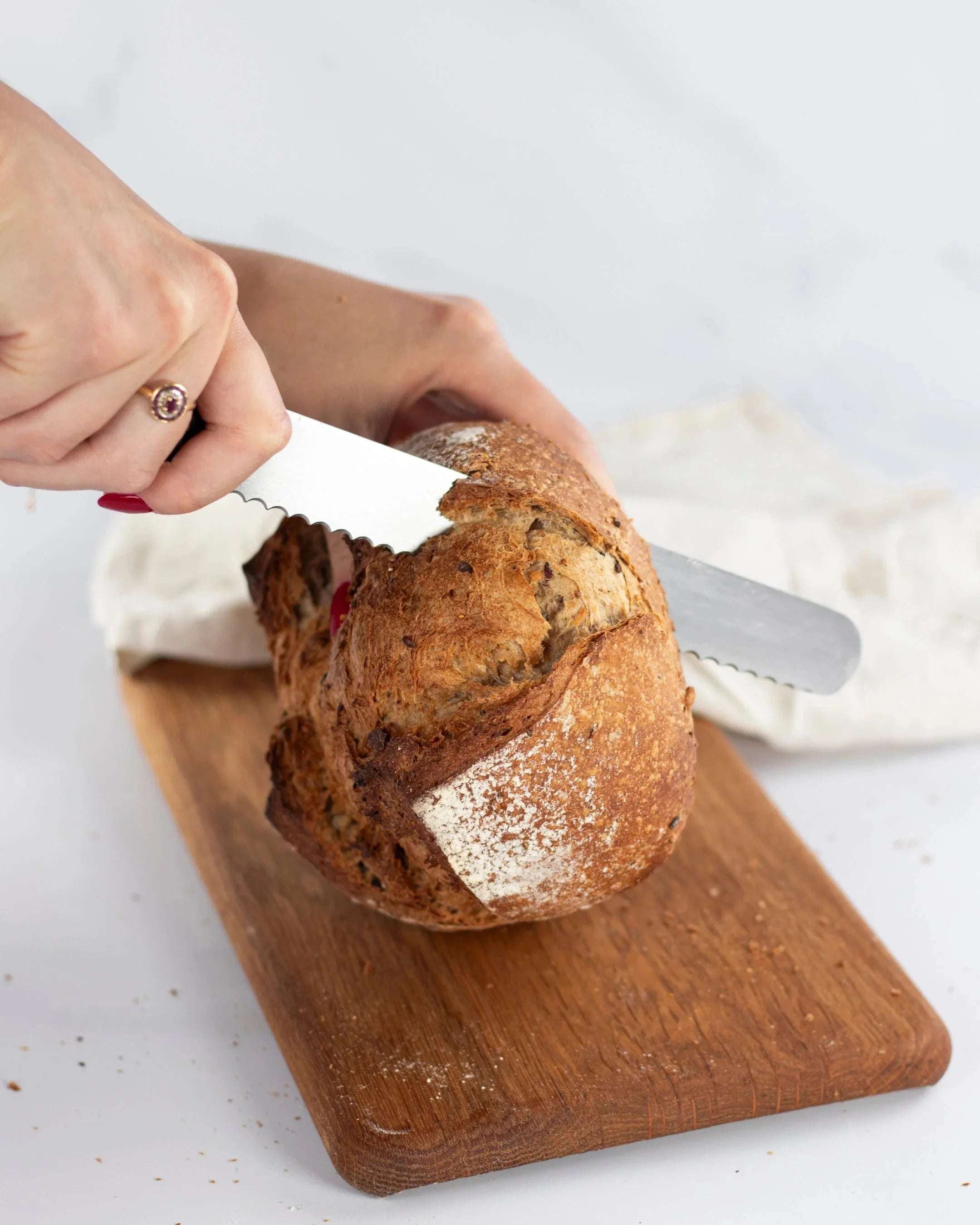 Une personne coupe un pain Bûcheron de Maison Vatelier avec un couteau à pain sur une planche.