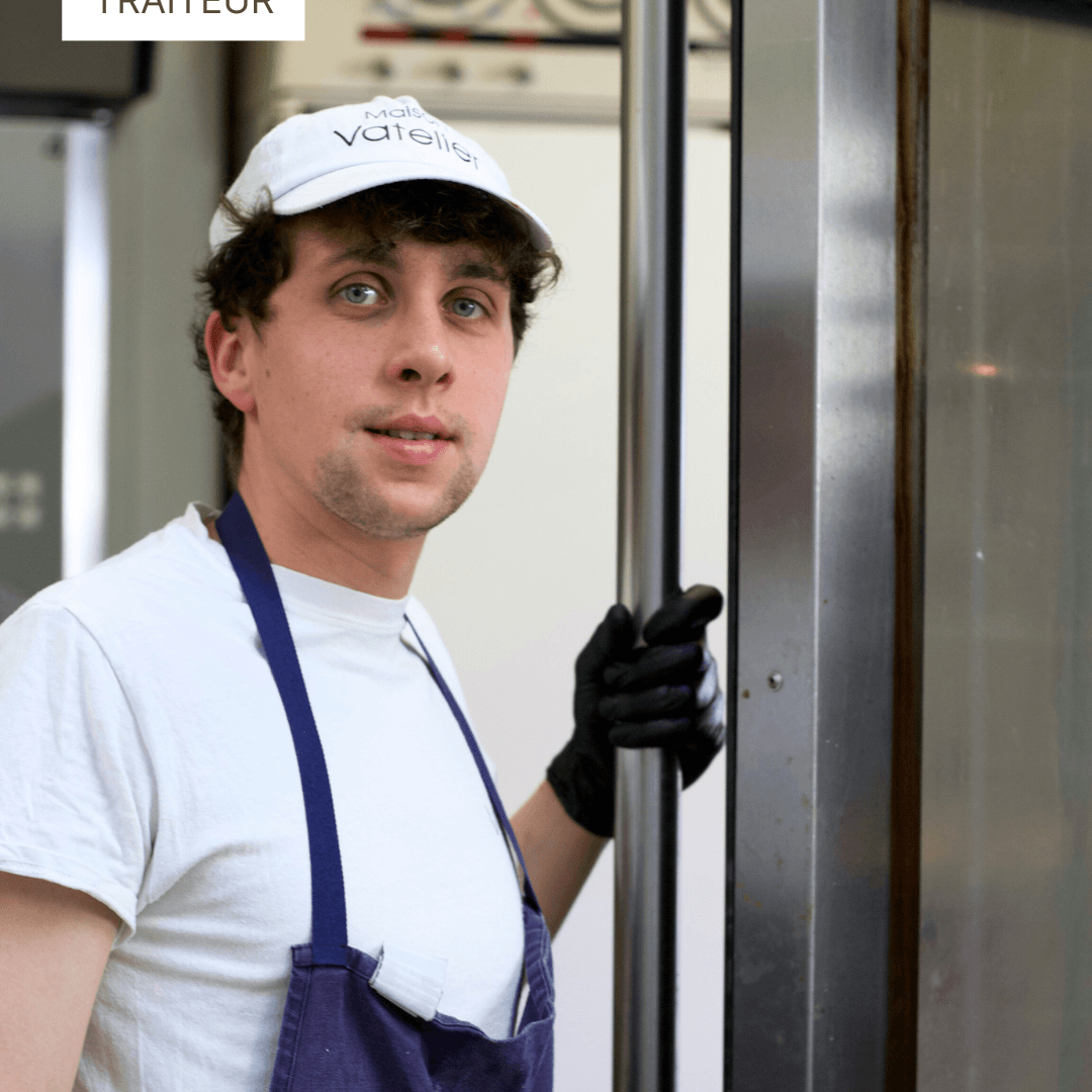Traiteur pâtissier en tenue de travail avec casquette et tablier bleu dans son atelier.