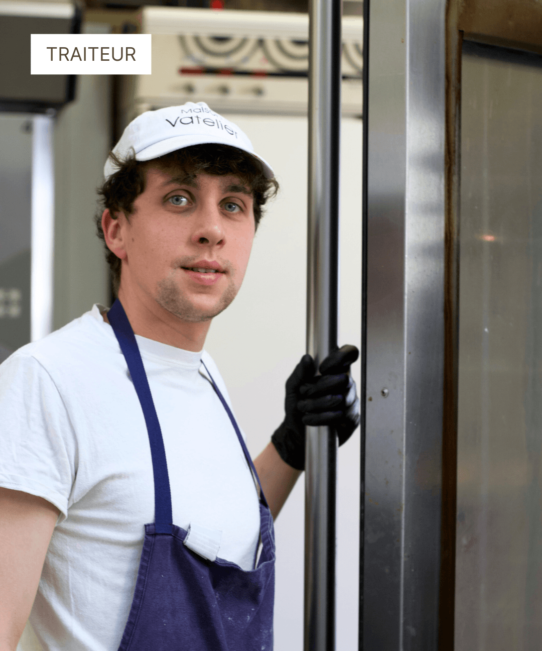 Traiteur pâtissier en tenue de travail avec casquette et tablier bleu dans son atelier.