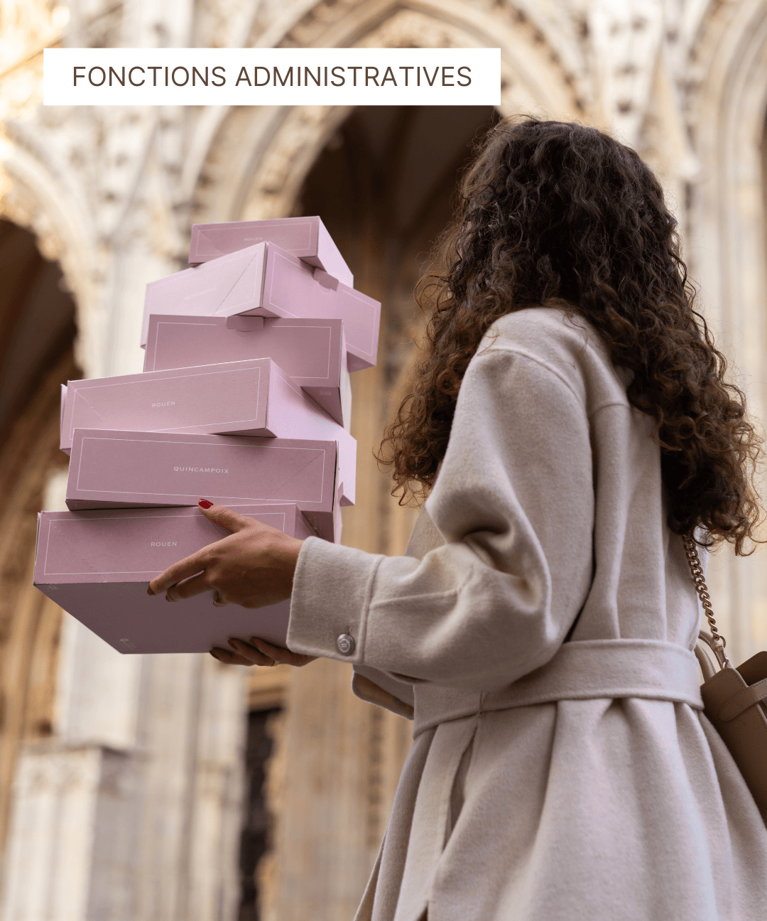 Femme portant une pile de boîtes à pâtisseries roses devant une architecture gothique.