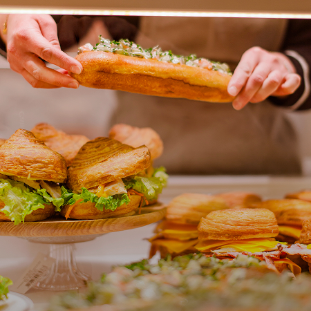 Boulanger préparant un sandwich baguette garni avec d'autres sandwiches artisanaux en vitrine