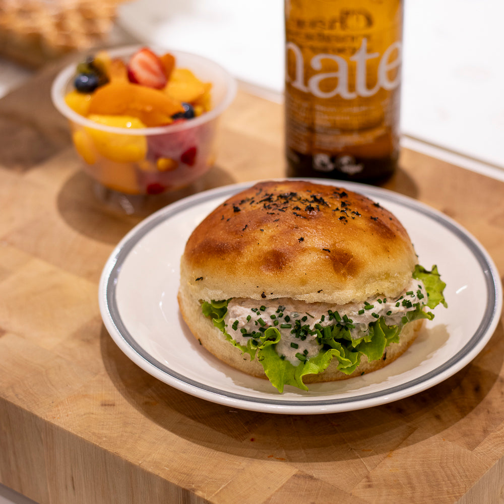 Sandwich gourmand au poulet et salade sur planche en bois avec salade de fruits et boisson.