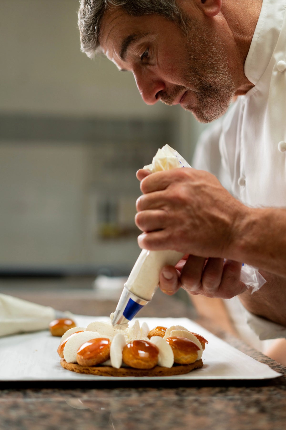 Un pâtissier dresse avec précision une crème sur un gâteau aux choux et caramel.