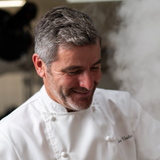Portrait souriant de Benoît Vatelier, pâtissier en veste blanche dans son atelier.