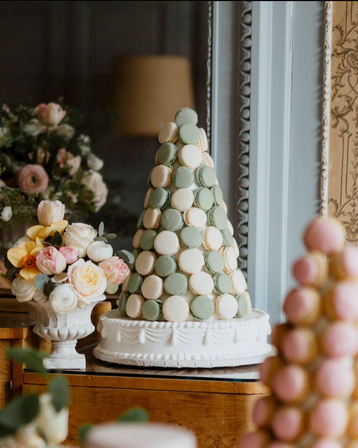 Pyramide de macarons vert pastel et crème sur un support blanc décoré