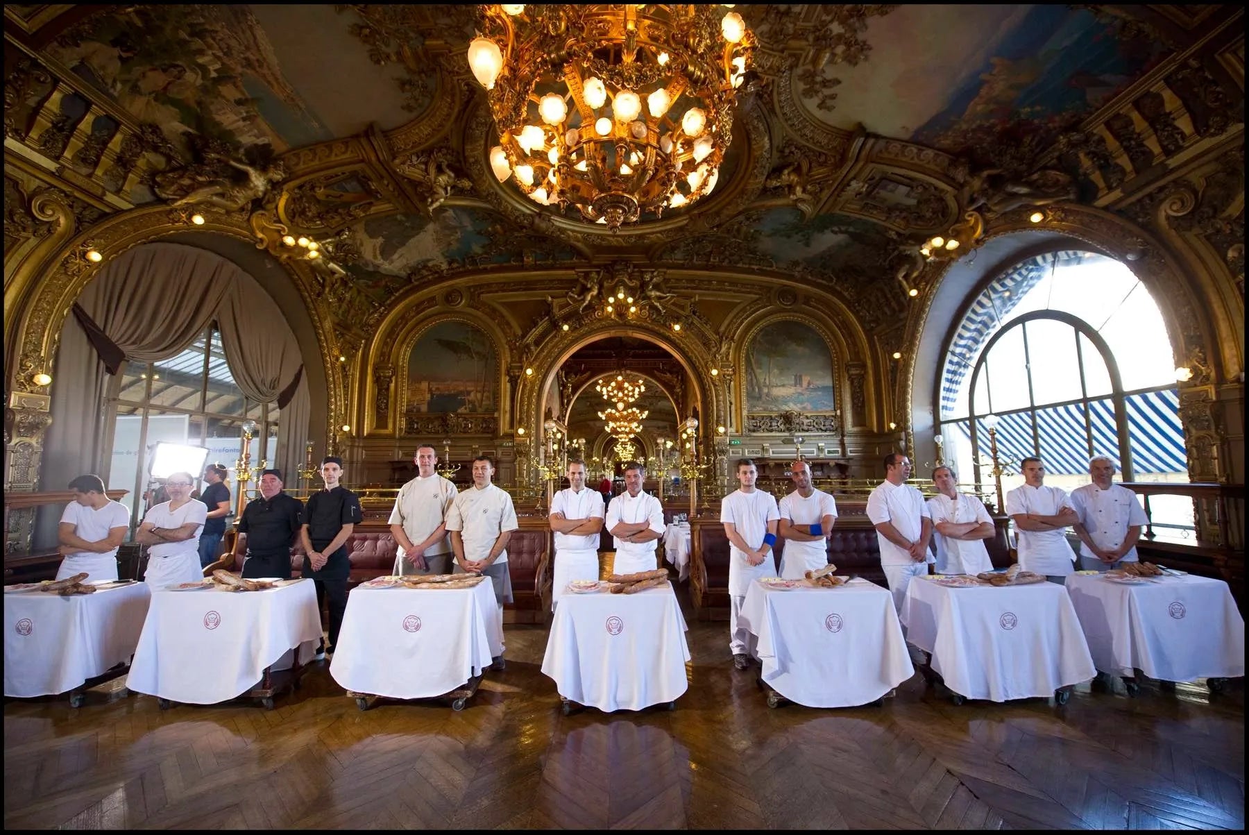 Une équipe de chefs pâtissiers alignée derrière des tables dressées dans un salon luxueux.