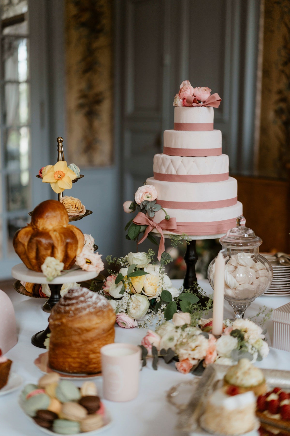 Buffet de pâtisseries avec un gâteau à étages rose, brioches et macarons.